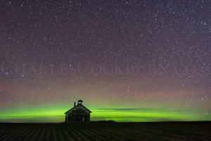 The aurora shines brightly behind an old schoolhouse.